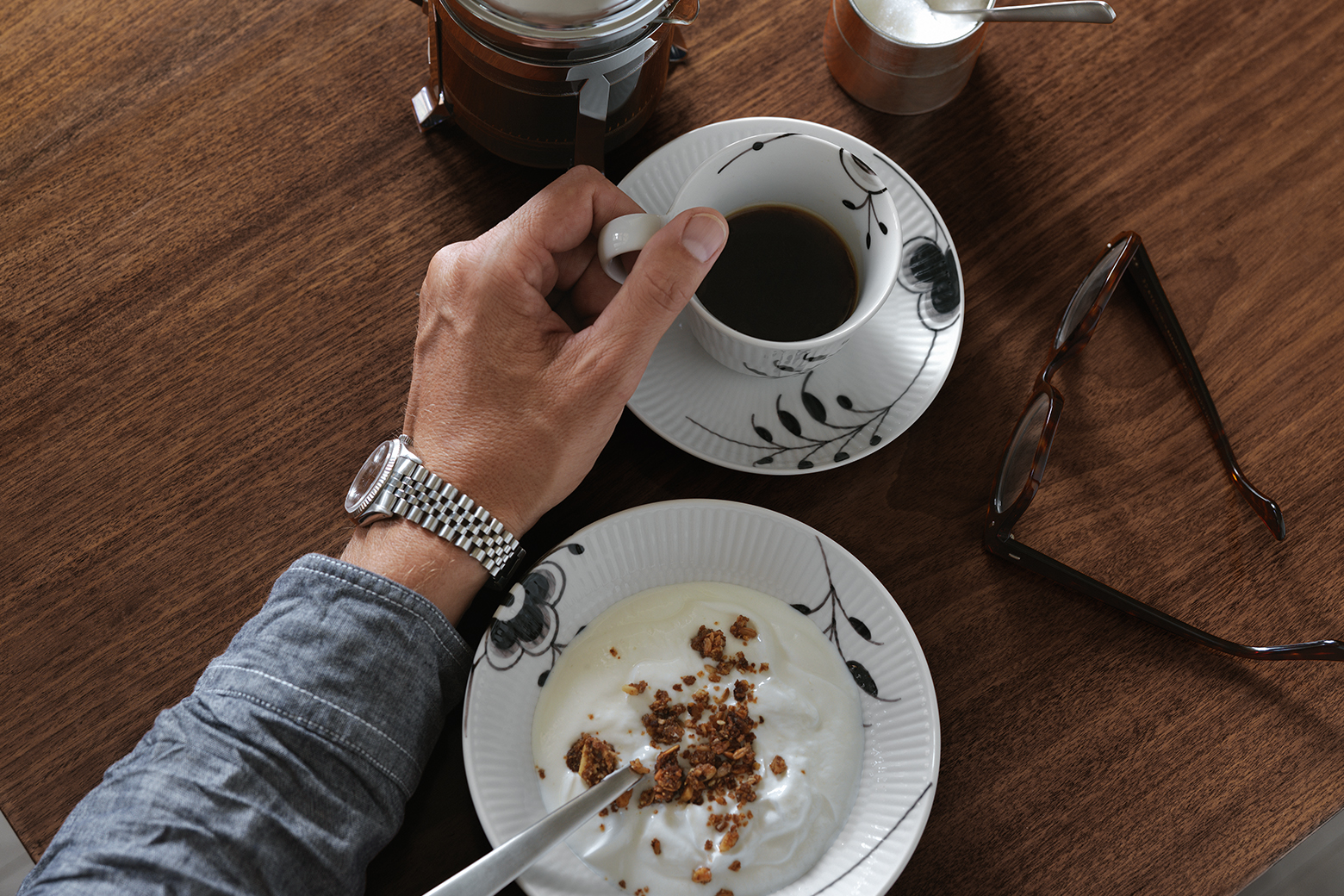A man enjoying breakfast eating yogurt out of a Black Fluted Mega Deep Plate and drinking coffee out of a Black Fluted Mega High Handle Cup